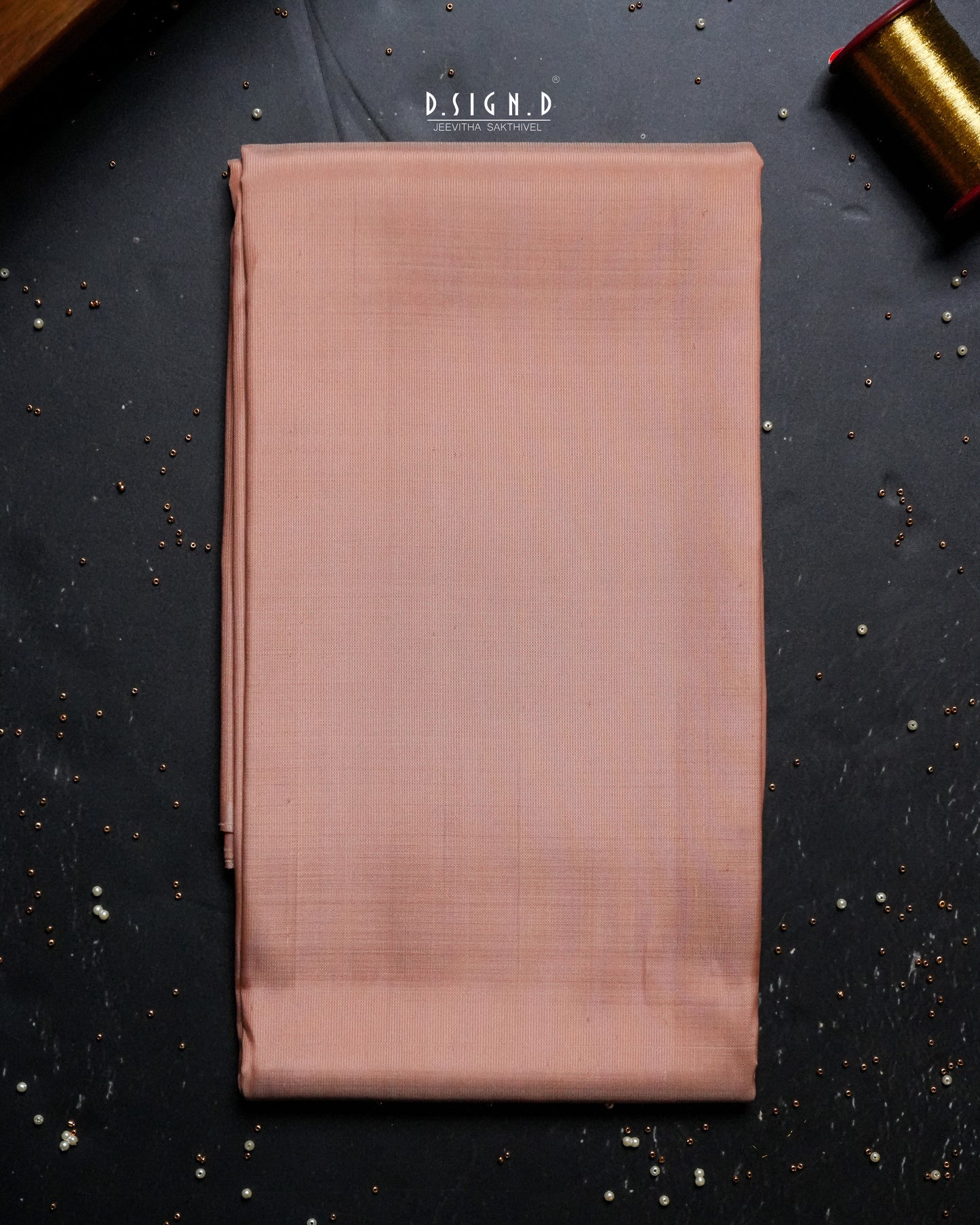 A folded copper shade fabric , likely a shirt material , is displayed flat on a dark textured background with decorative gold props in the corners.