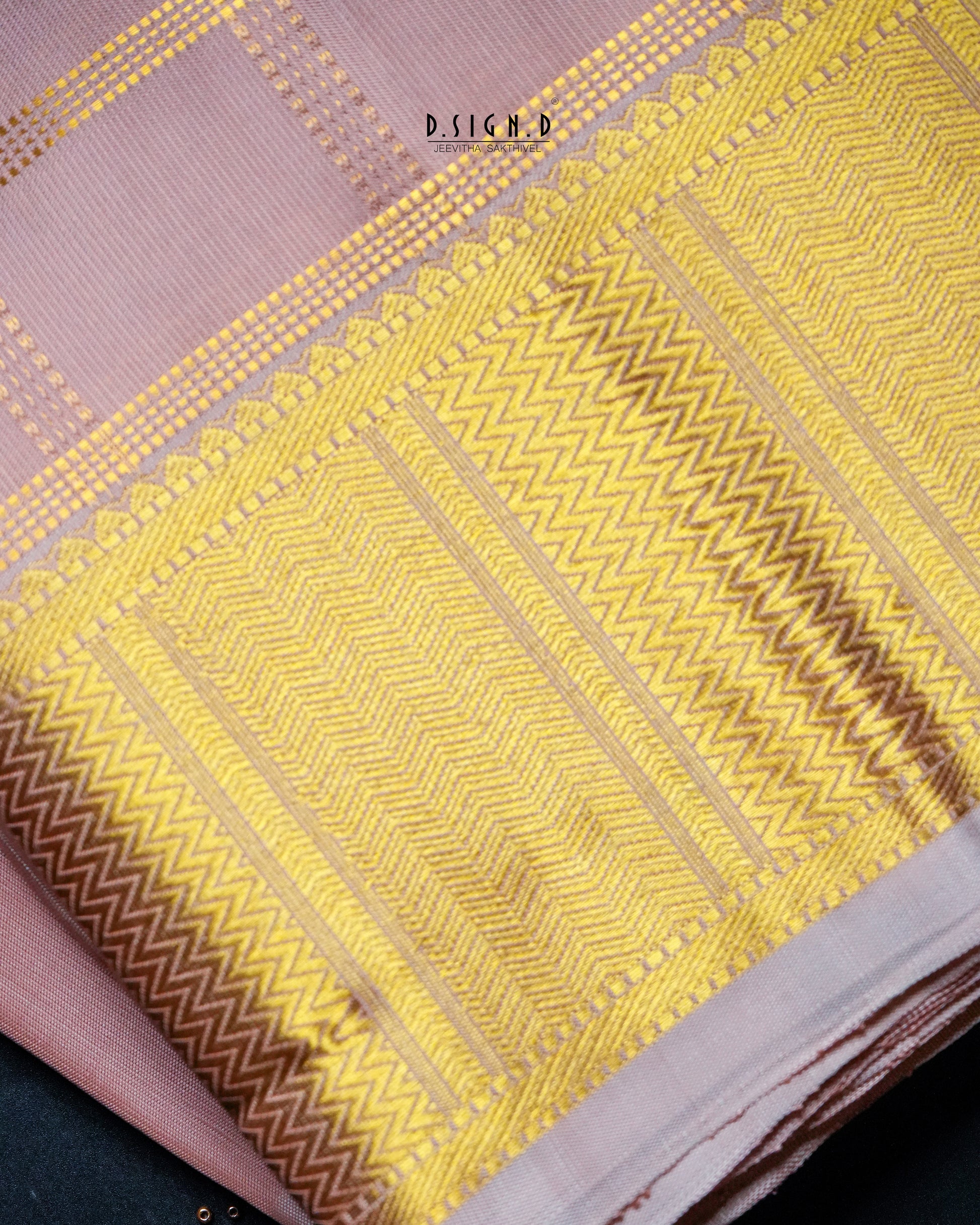 A close-up of a copper and yellow patterned fabric, likely a dhoti, featuring intricate gold woven geometric designs and a border.