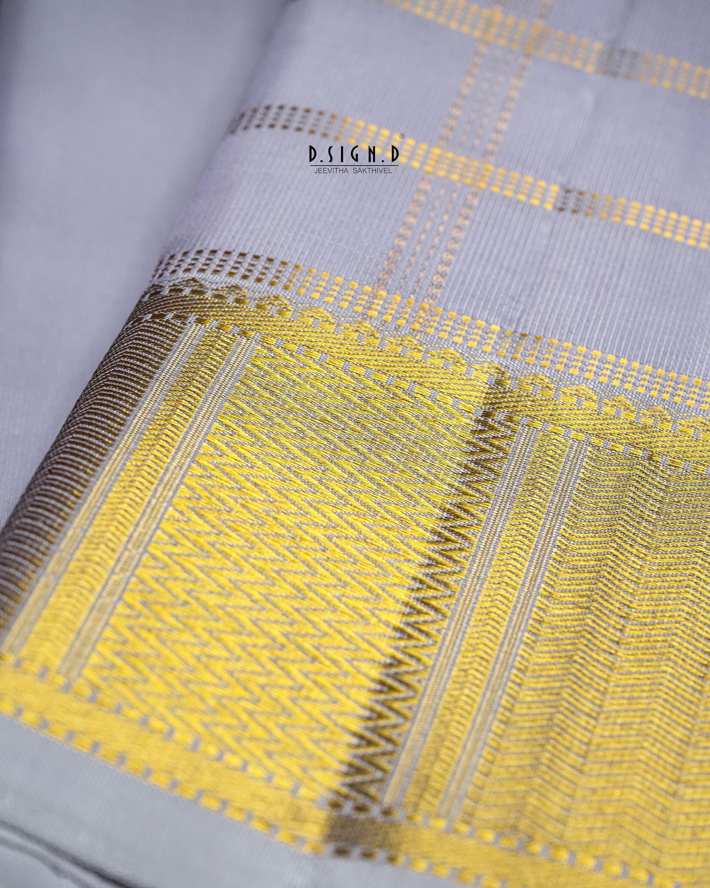 A close-up of a mauve shade dhoti with a wide yellow and gold woven border featuring geometric patterns and fine stripes. 