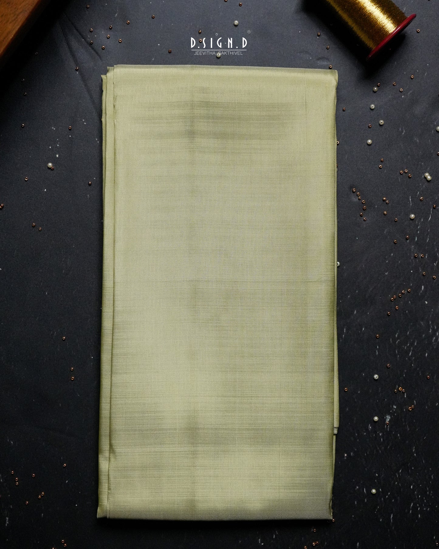 A folded piece of pista green shirt fabric laid flat on a dark textured surface, with a spool of matching thread partially visible in the top right corner.
