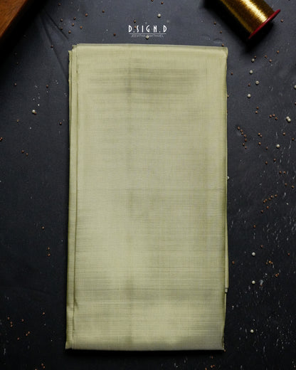 A folded piece of pista green shirt fabric laid flat on a dark textured surface, with a spool of matching thread partially visible in the top right corner.