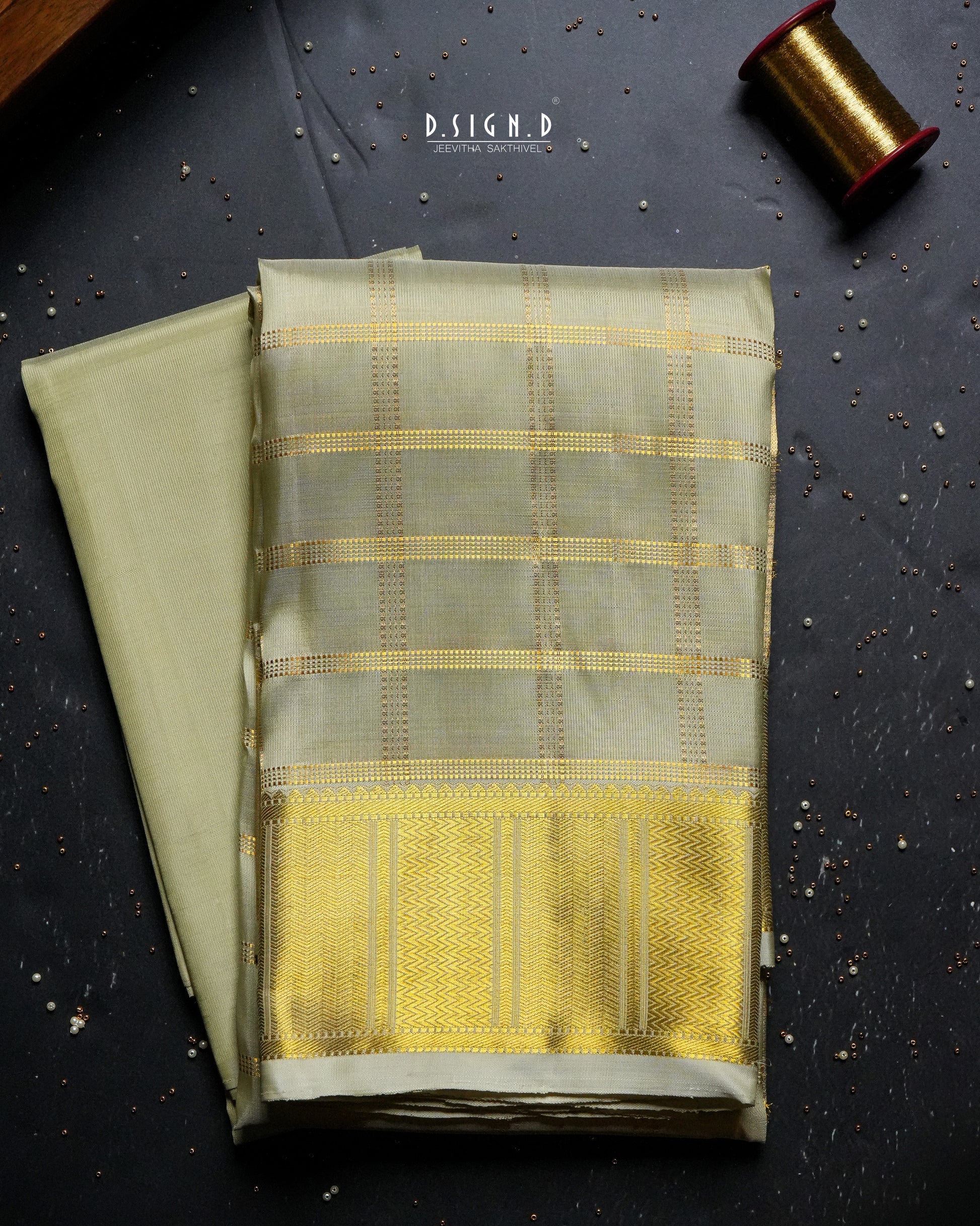 A folded light pista green dhoti  with a wide golden-yellow border and subtle woven stripes & a plain shirt material, displayed on a dark textured surface with a spool of thread in the corner.