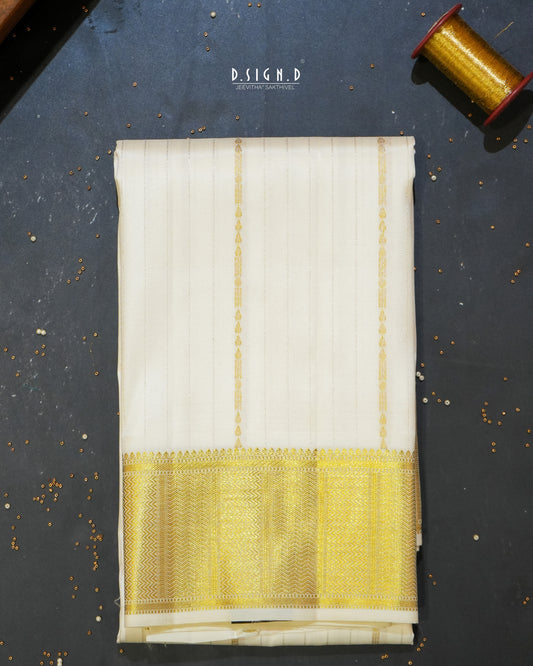 A folded white colored silk dhoti with a wide yellow and gold zari border, displayed on a dark textured surface with a spool of gold thread in the top right corner.