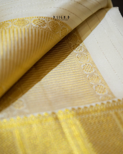 A close-up of a folded white and yellow woven fabric, showing detailed texture, fine stripes, and a decorative border pattern.