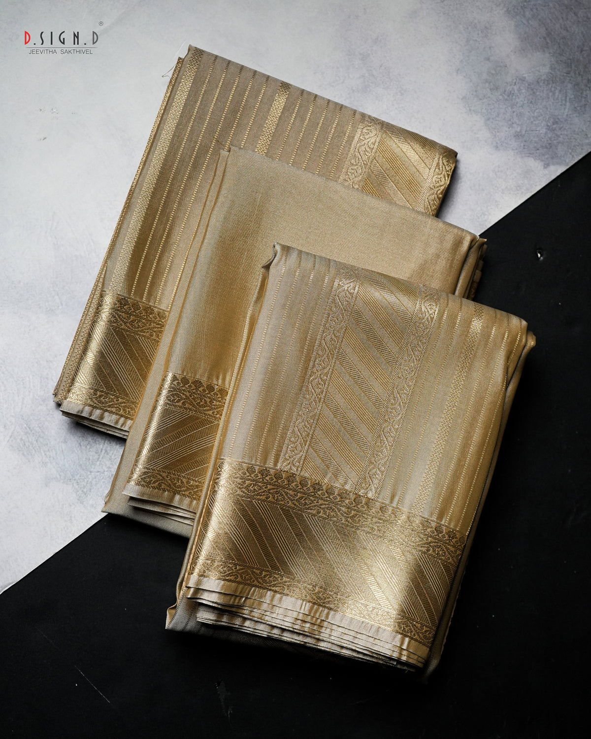 Three folded pieces of metallic gold fabric with woven geometric borders, arranged diagonally on a split light gray and black background. 