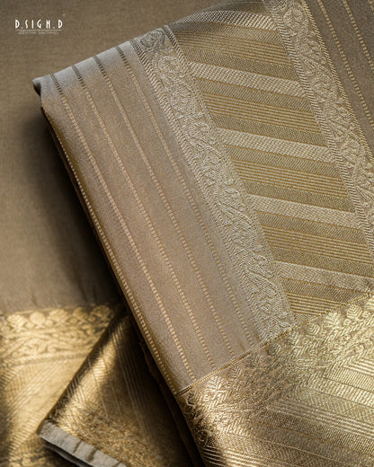A close-up of a folded woven fabric, likely a textile, showing metallic gold and beige patterns with a subtle sheen. The fabric features vertical stripes, woven floral borders, and geometric designs.