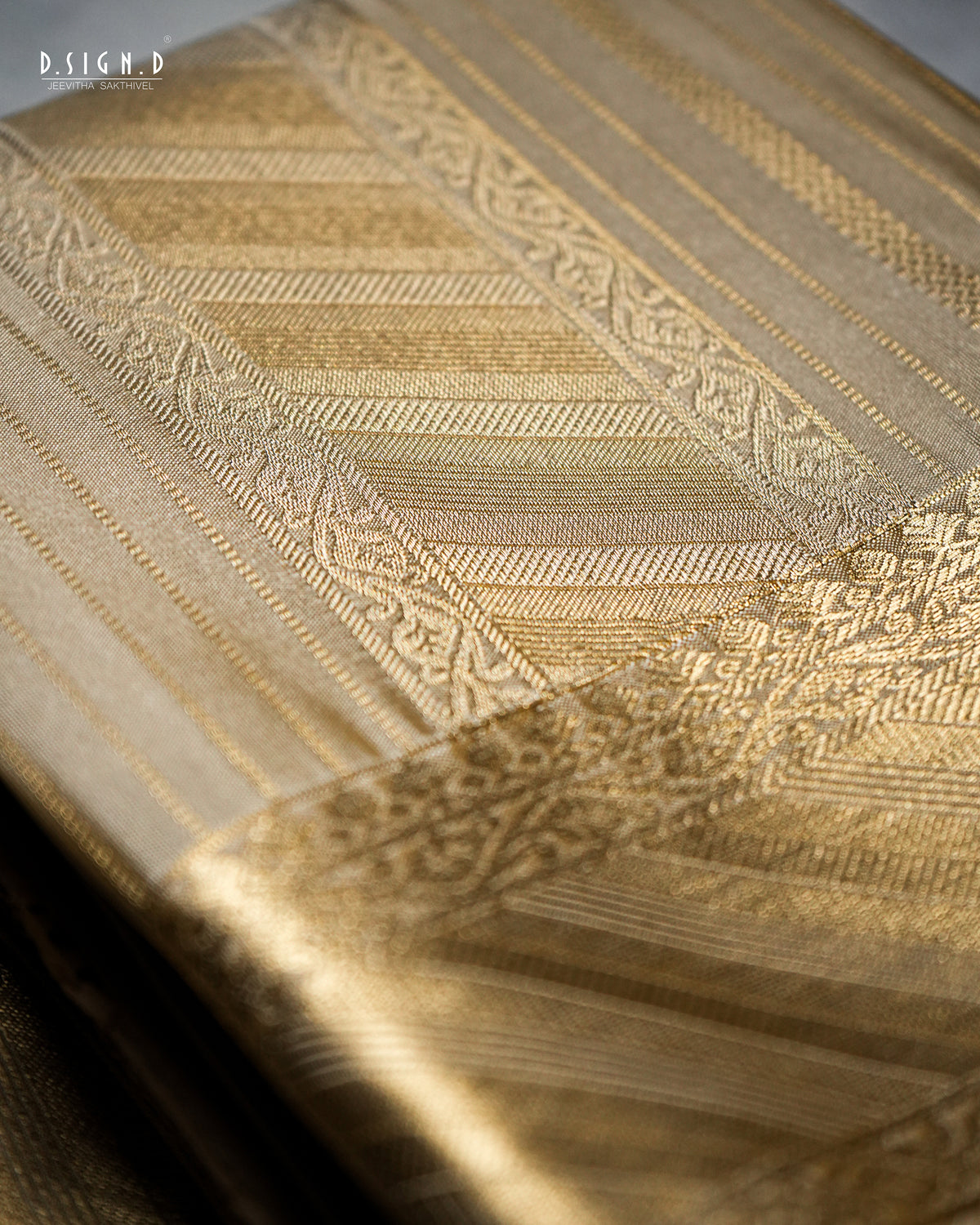 A close-up of a luxurious woven fabric,  featuring intricate gold and beige geometric patterns and borders. The fabric is draped elegantly, highlighting its rich texture and sheen under warm lighting.