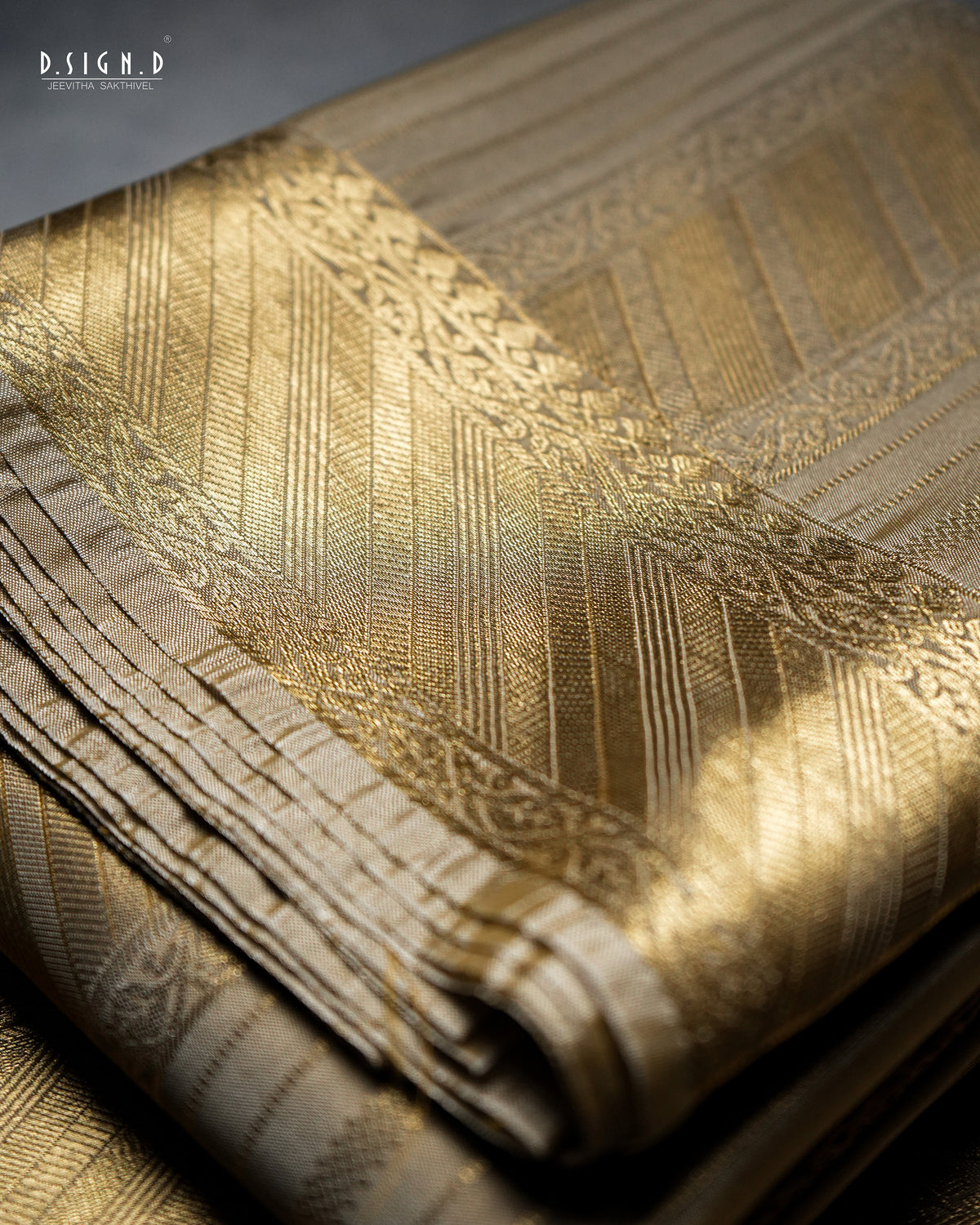 A close-up of a folded gold and beige patterned fabric, showing intricate woven stripes and borders under warm directional light. 