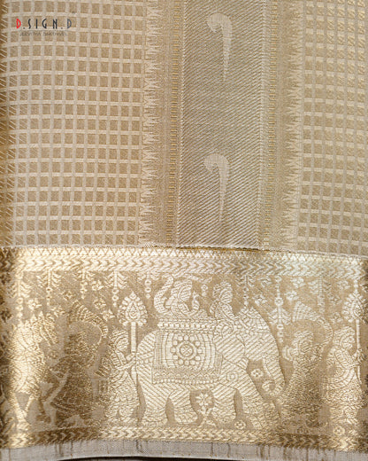 A close-up of a beige and gold woven fabric, likely a dhoti body or decorative textile, featuring a detailed gold zari brocade border with traditional motifs and a grid pattern.