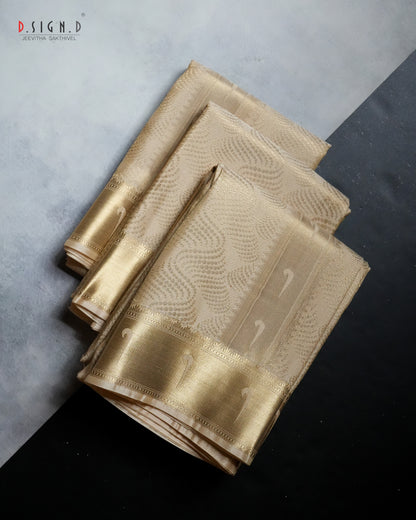 A folded gold silk dhoti set with a metallic gold border and subtle woven patterns, displayed on a split gray and black background. 