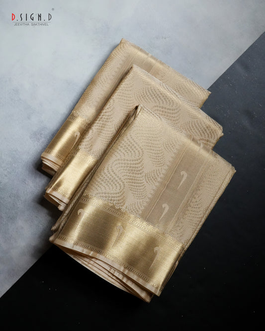 A folded gold silk dhoti set with a metallic gold border and subtle woven patterns, displayed on a split gray and black background. 