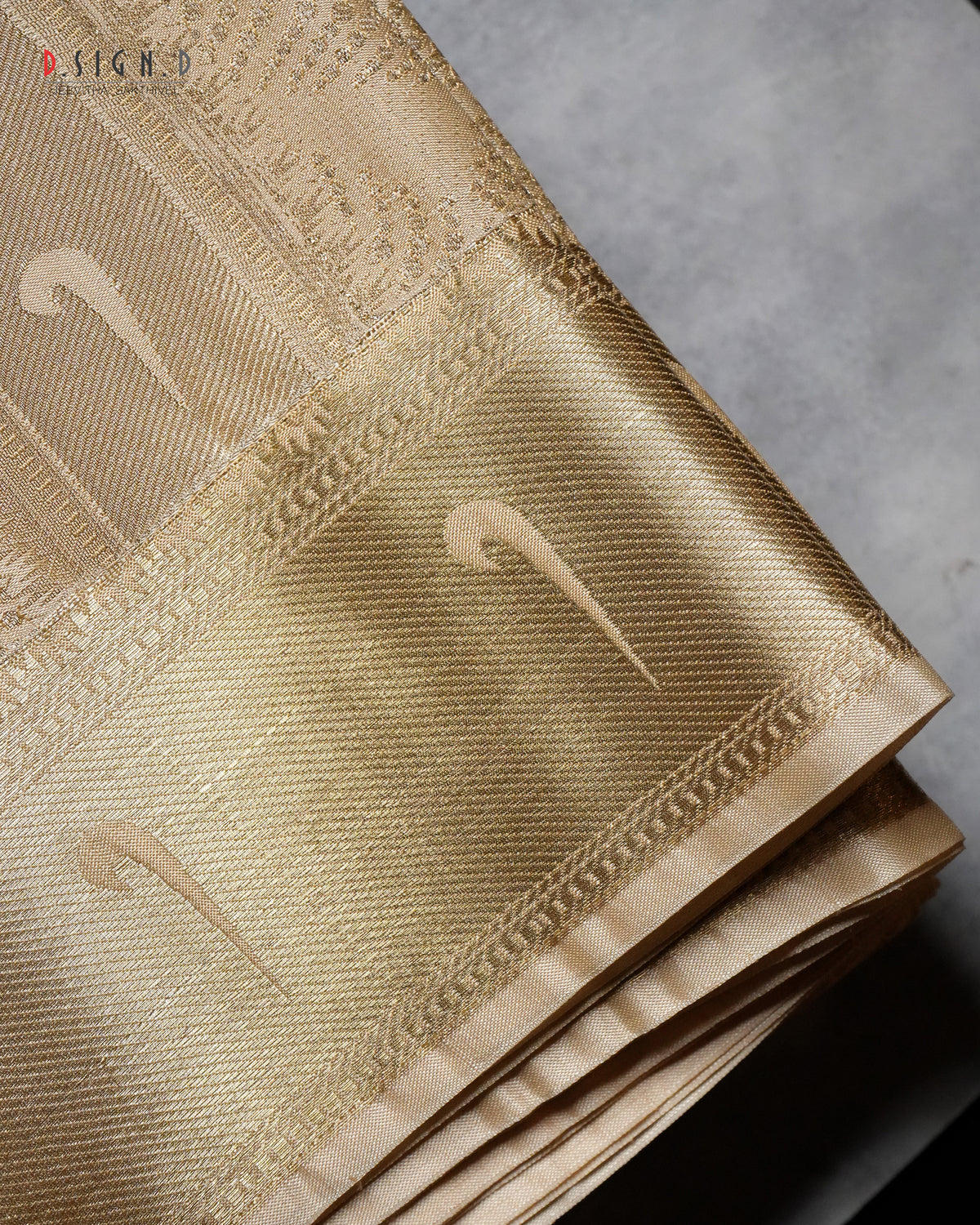 A close-up of a folded gold silk fabric with a textured weave and subtle woven motifs, set against a neutral gray background.