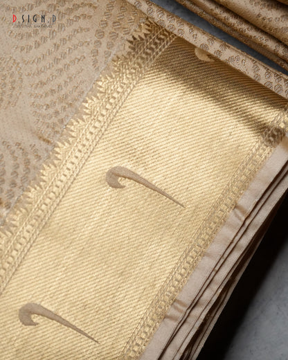 A close-up of a gold patterned fabric, likely a dhoti, showing detailed woven textures, borders, and subtle gold motifs.