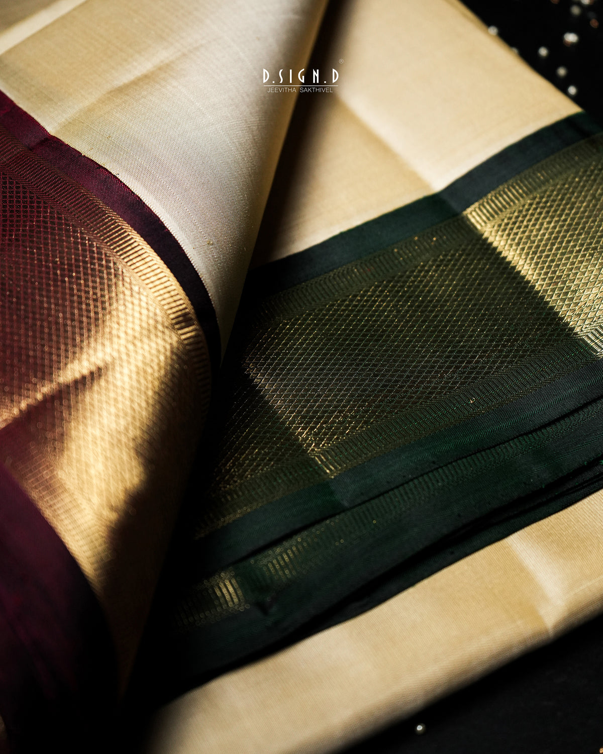 A close-up of a folded silk dhoti or fabric with a cream body, a deep green border, a metallic gold border, and a dark plum border.