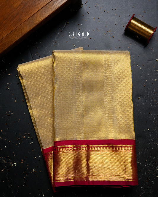 Folded gold silk dhoti with a red zari border, styled on a dark surface with thread and a wooden box.