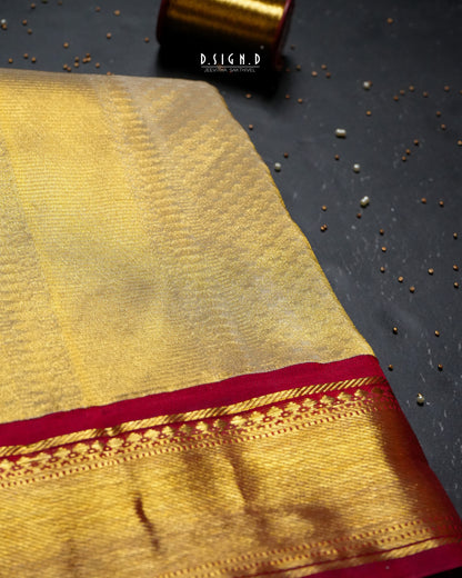 Close-up of a gold silk dhoti with a deep red zari border, styled on a dark surface with beads and a spool.