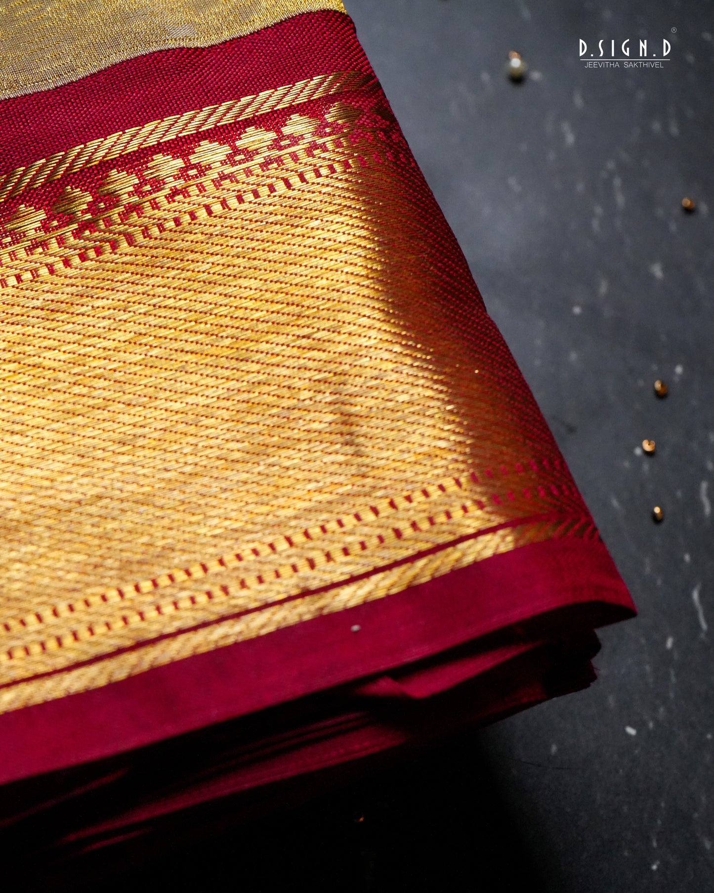 Folded gold and deep red zari silk dhoti, displayed on a dark textured background.