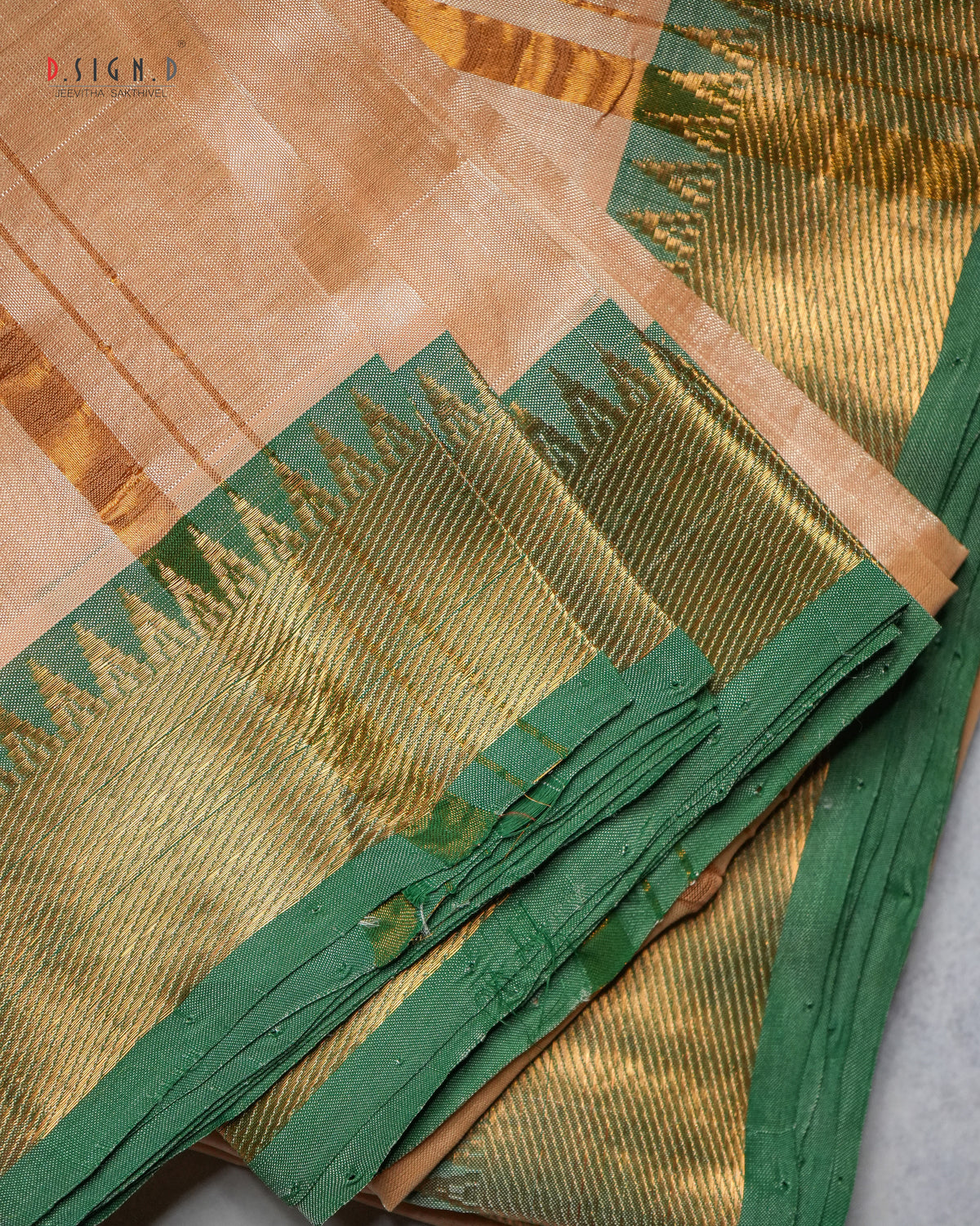 A close-up of a traditional Indian silk dhoti with a beige body, a wide green border, and intricate gold zari metallic weaving.