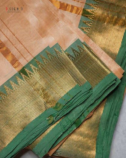 A close-up of a traditional Indian silk dhoti with a beige body, a wide green border, and intricate gold zari metallic weaving.