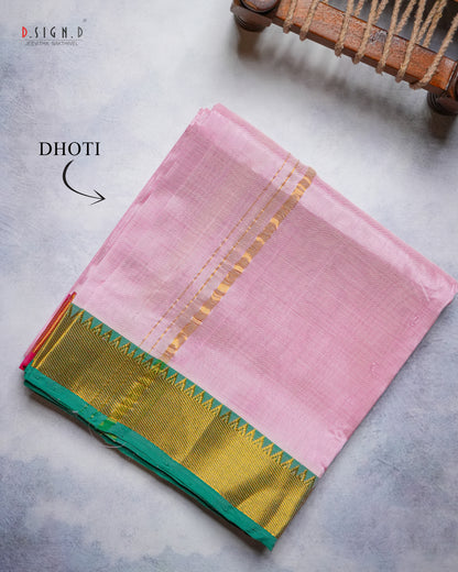 A folded pink silk Dhoti with a green and gold border, displayed on a textured gray surface with a wooden prop in the corner.