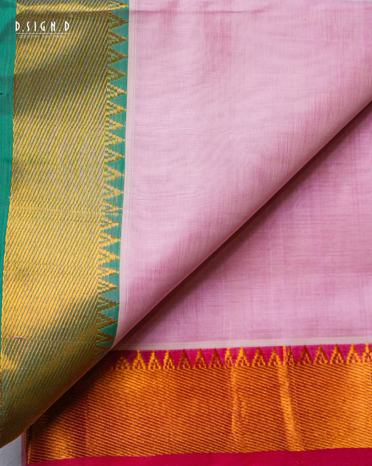 A close-up of a pink silkdhoti & vastram with a gold and green zari border and a metallic orange-gold pallu, folded to show its texture and pattern.