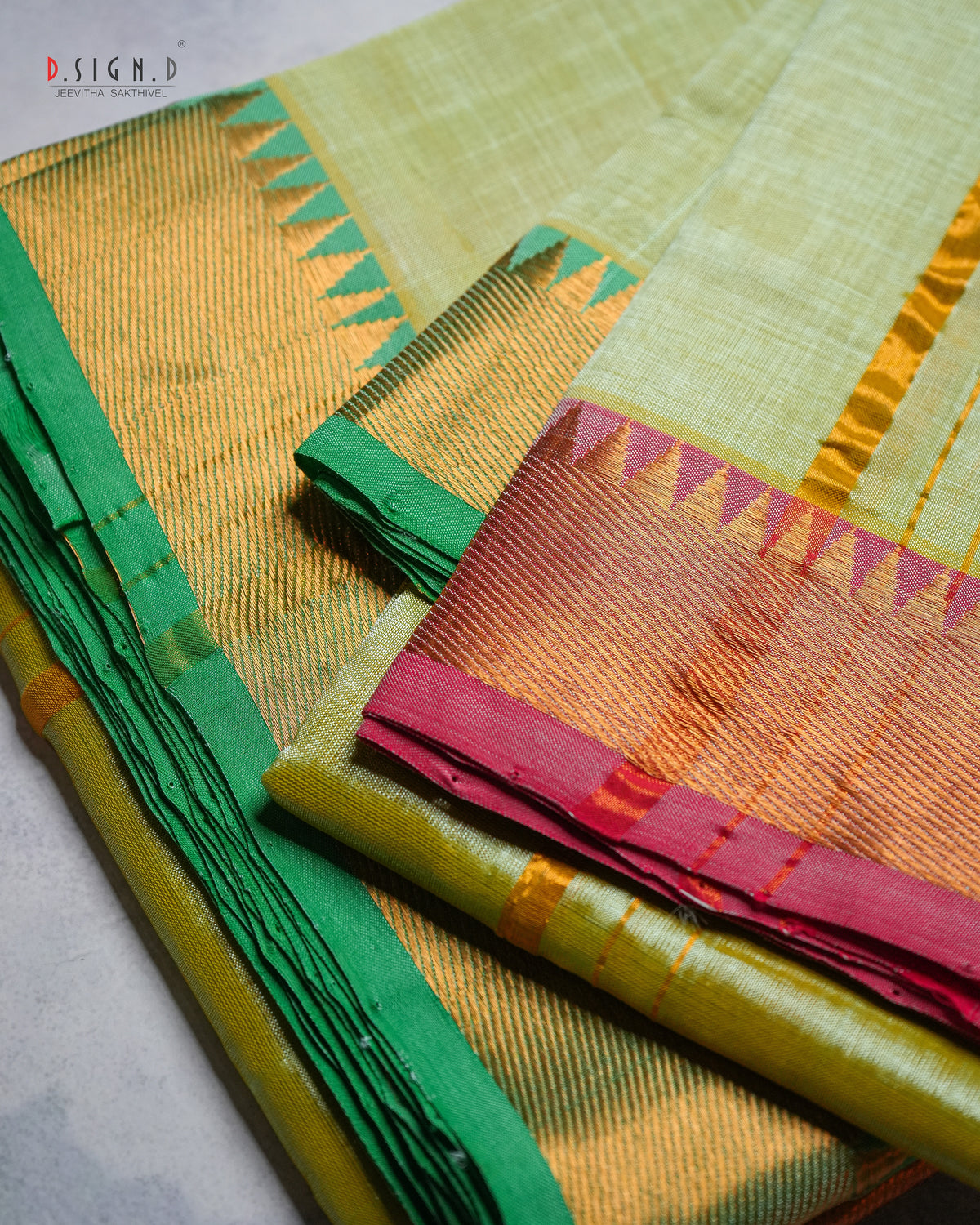 A folded and draped silk dhoti with a light green body, a vibrant green border, and a golden-yellow zari-embellished pallu section with pink and orange accents. 