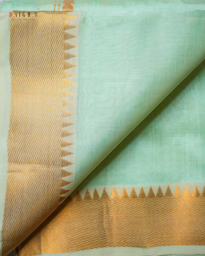 A close-up of a mint green silk dhoti & vastram with a wide gold zari border featuring a triangular pattern.