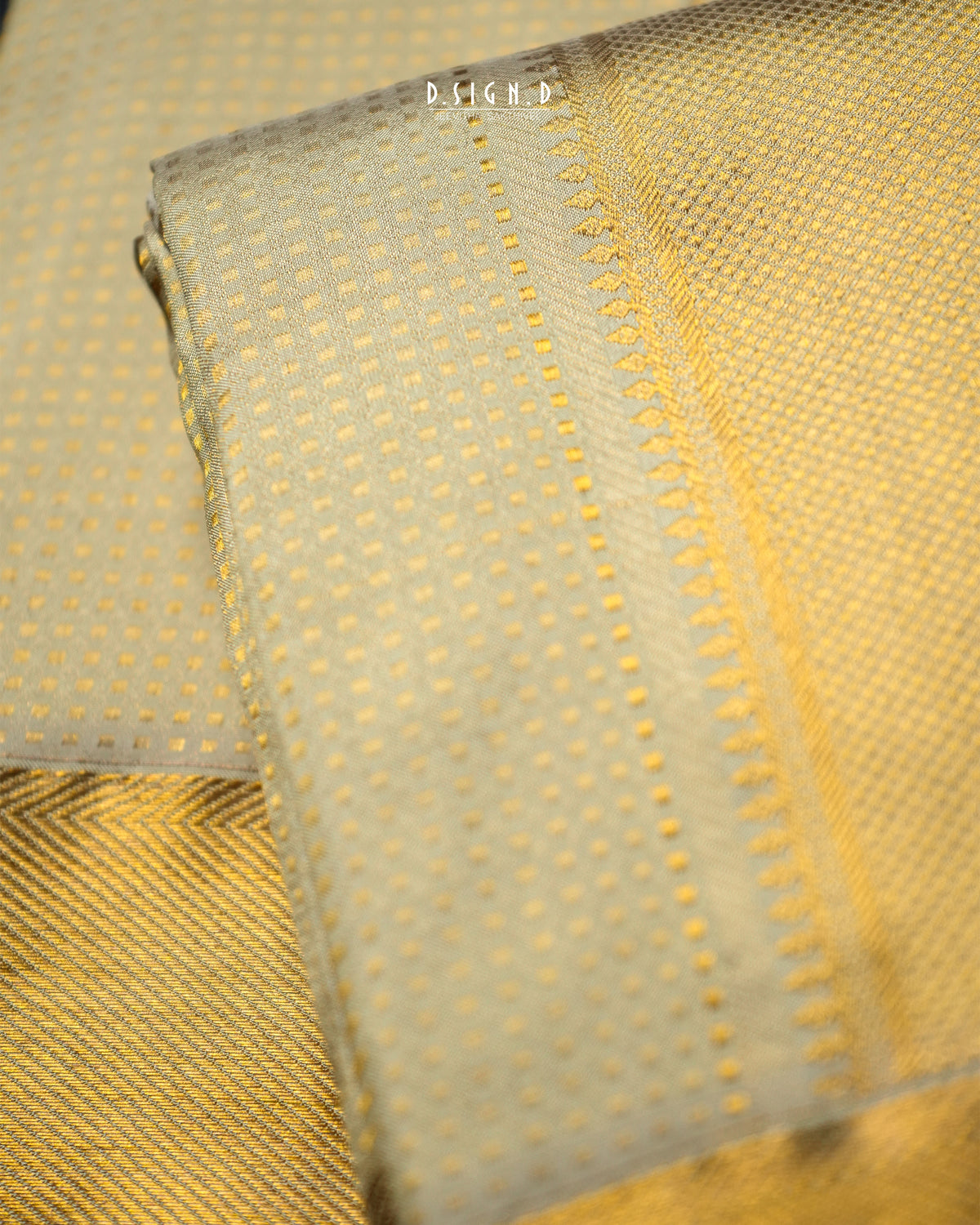A close-up of a folded light pista green dhoti set with a fine gold dotted pattern and a decorative gold border, shown against a matching textured fabric background.