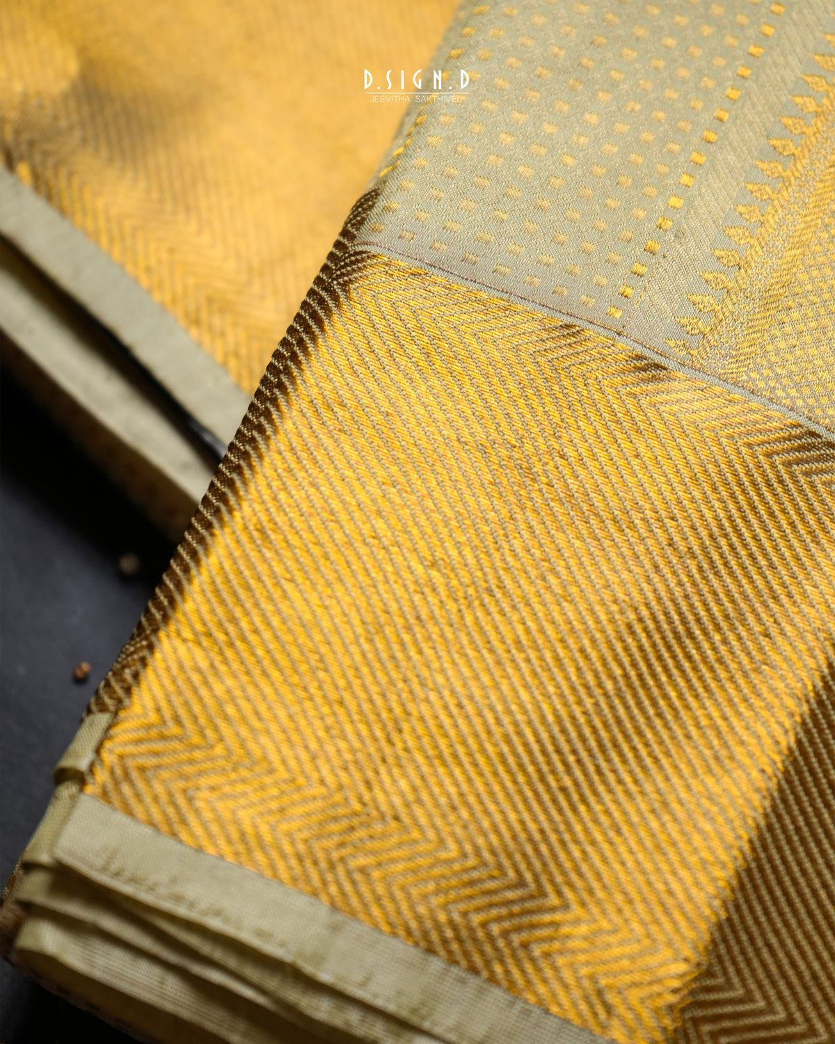 A close-up of a folded golden-yellow fabric, likely a dhoti, showing detailed woven patterns, a border.