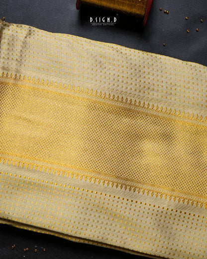 A folded piece of light pista green dhoti set with a fine dotted pattern and decorative woven borders, displayed on a dark textured surface with a small branded tag visible near the top.