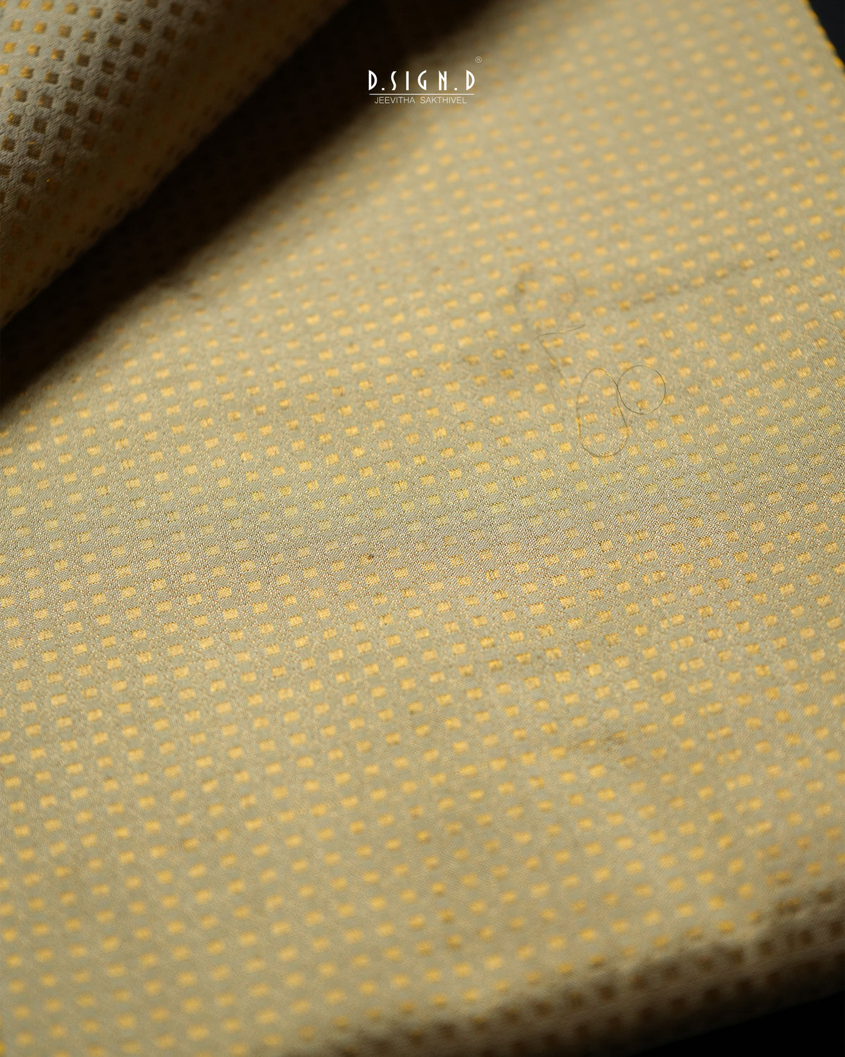 A close-up of a textured fabric with a fine dotted pattern in pale pista green, with a folded corner revealing the reverse side. 