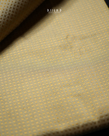 A close-up of a textured fabric with a fine dotted pattern in pale pista green, with a folded corner revealing the reverse side. 