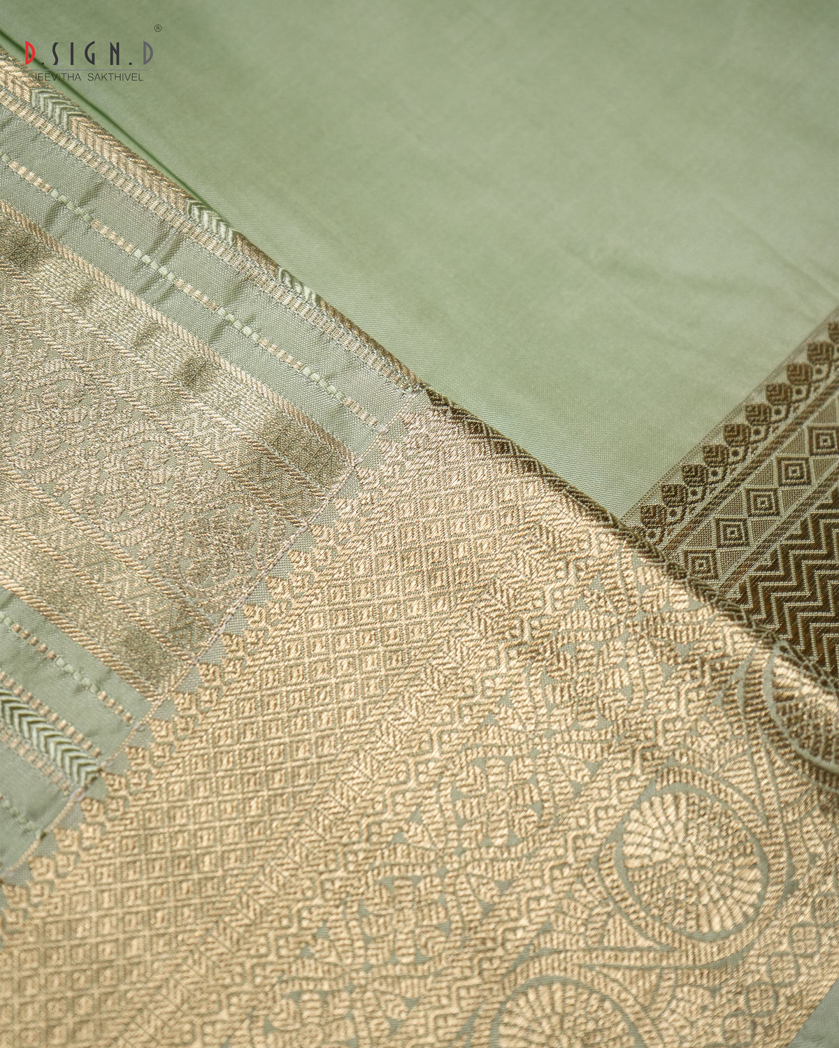 A close-up of a light sage green fabric, likely silk or satin, featuring an ornate gold brocade border with geometric and floral patterns.