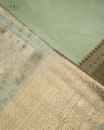 A close-up of a light sage green fabric, likely silk or satin, featuring an ornate gold brocade border with geometric and floral patterns.