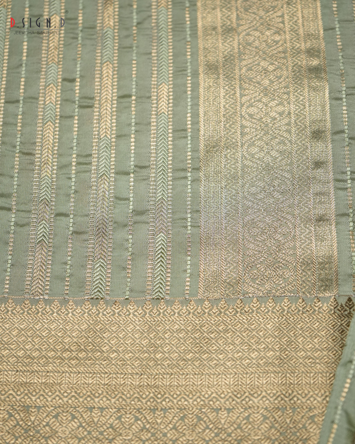 A close-up of a woven fabric, likely a silk dhoti, featuring a sage green body with vertical stripes of gold and beige zari motifs, and a wide gold brocade border at the bottom.