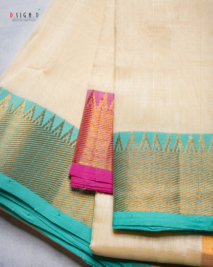 A folded cream-colored silk dhoti with a vibrant teal border and a pink and gold zari woven accent panel, displayed on a light gray surface.
