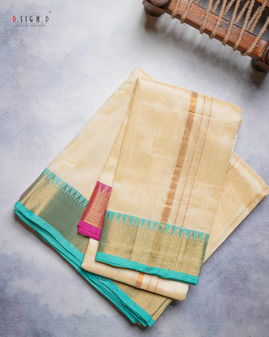A folded beige silk dhoti with a wide teal border and gold zari stripes, displayed on a textured gray surface with a wooden object partially visible in the top right corner.