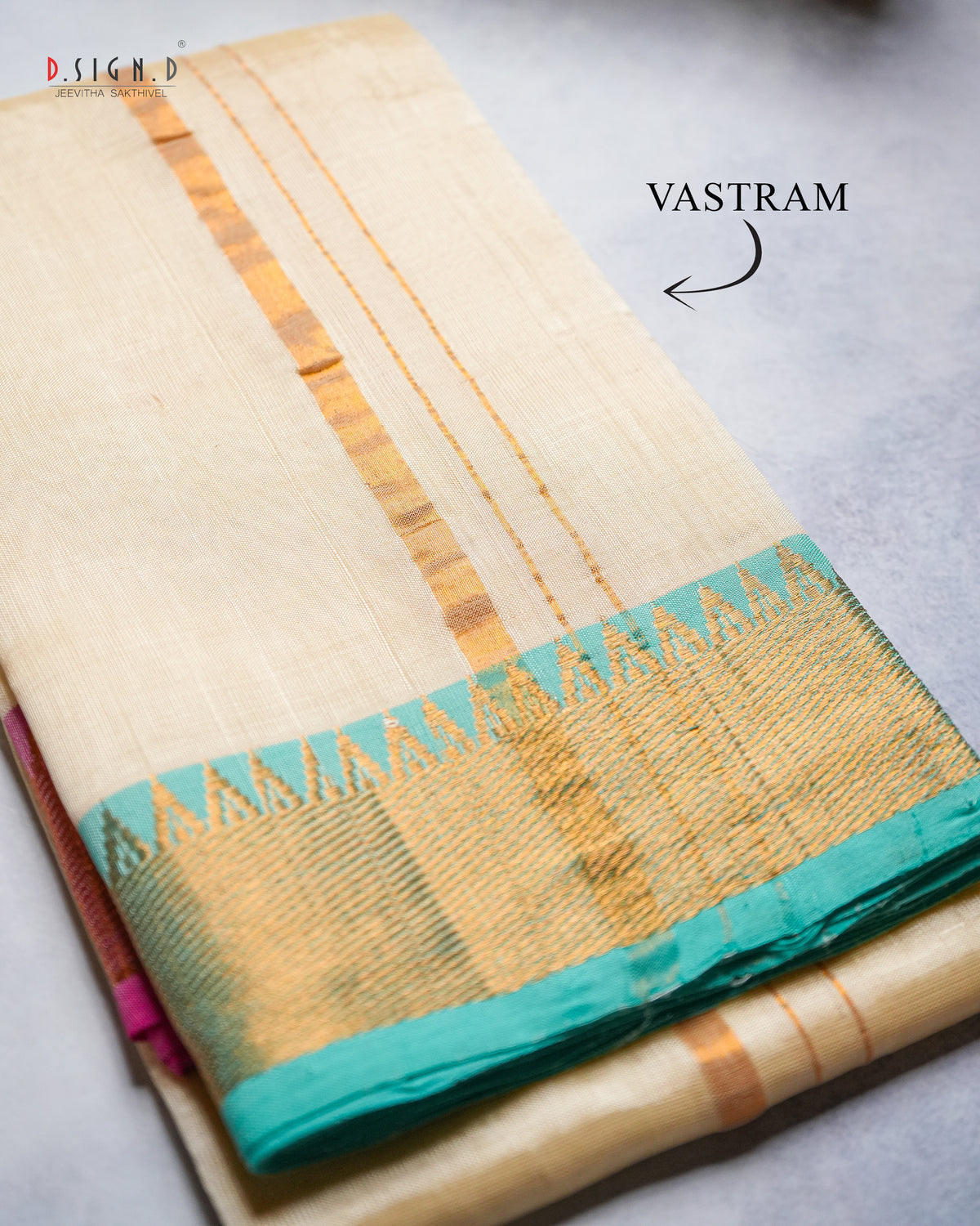 A folded cream-colored silk vastram with gold zari stripes and a teal border.
