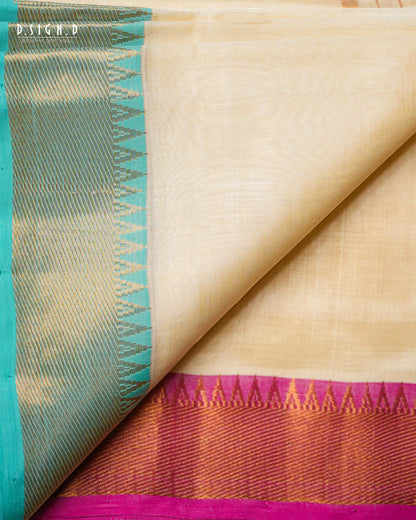 A close-up of a folded cream-colored silk dhoti with a prominent teal border and a magenta and gold zari decorative pallu.