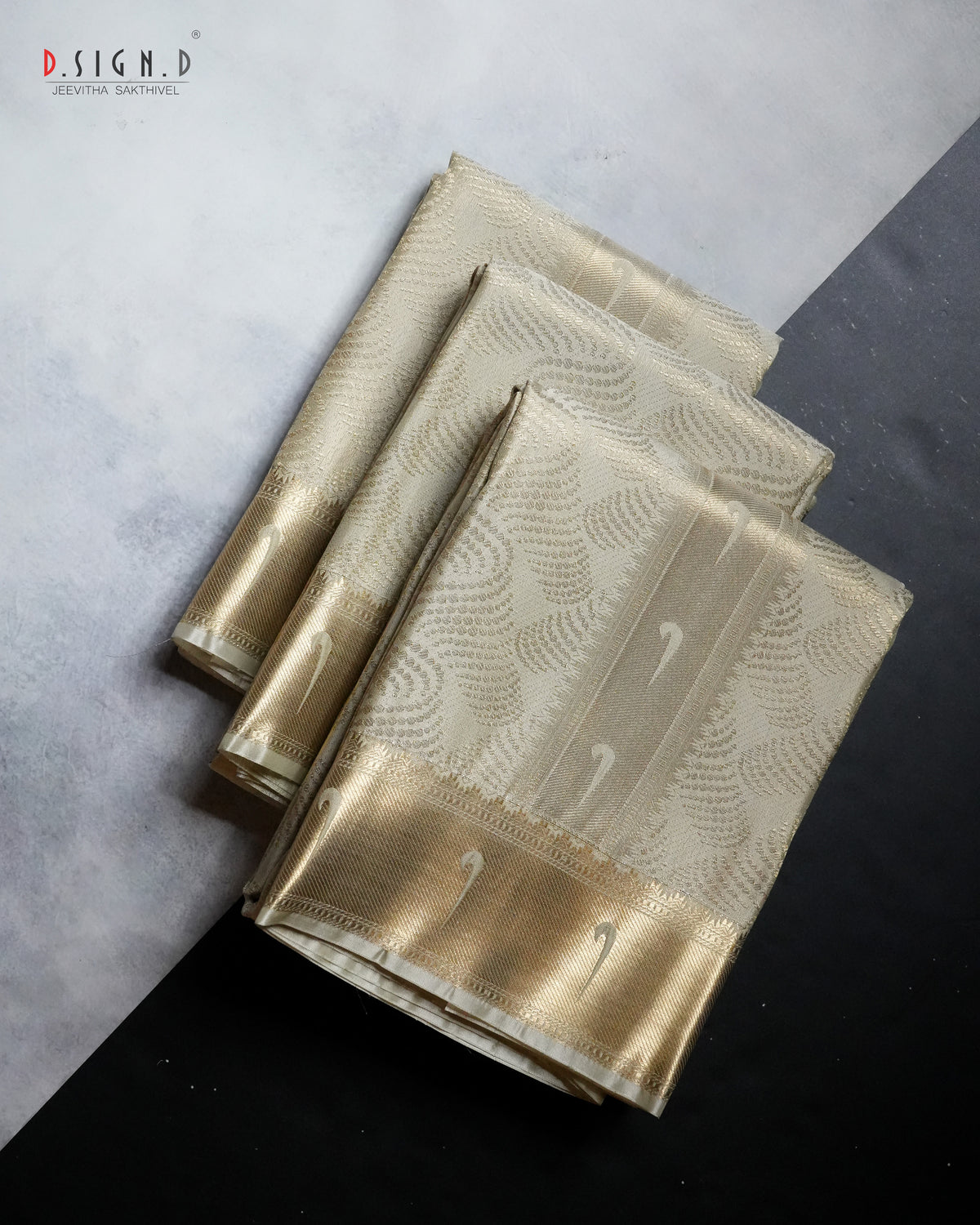 Three folded dhoti set with a metallic gold and pista green floral pattern and wide gold borders, arranged diagonally on a split gray and black background. 
