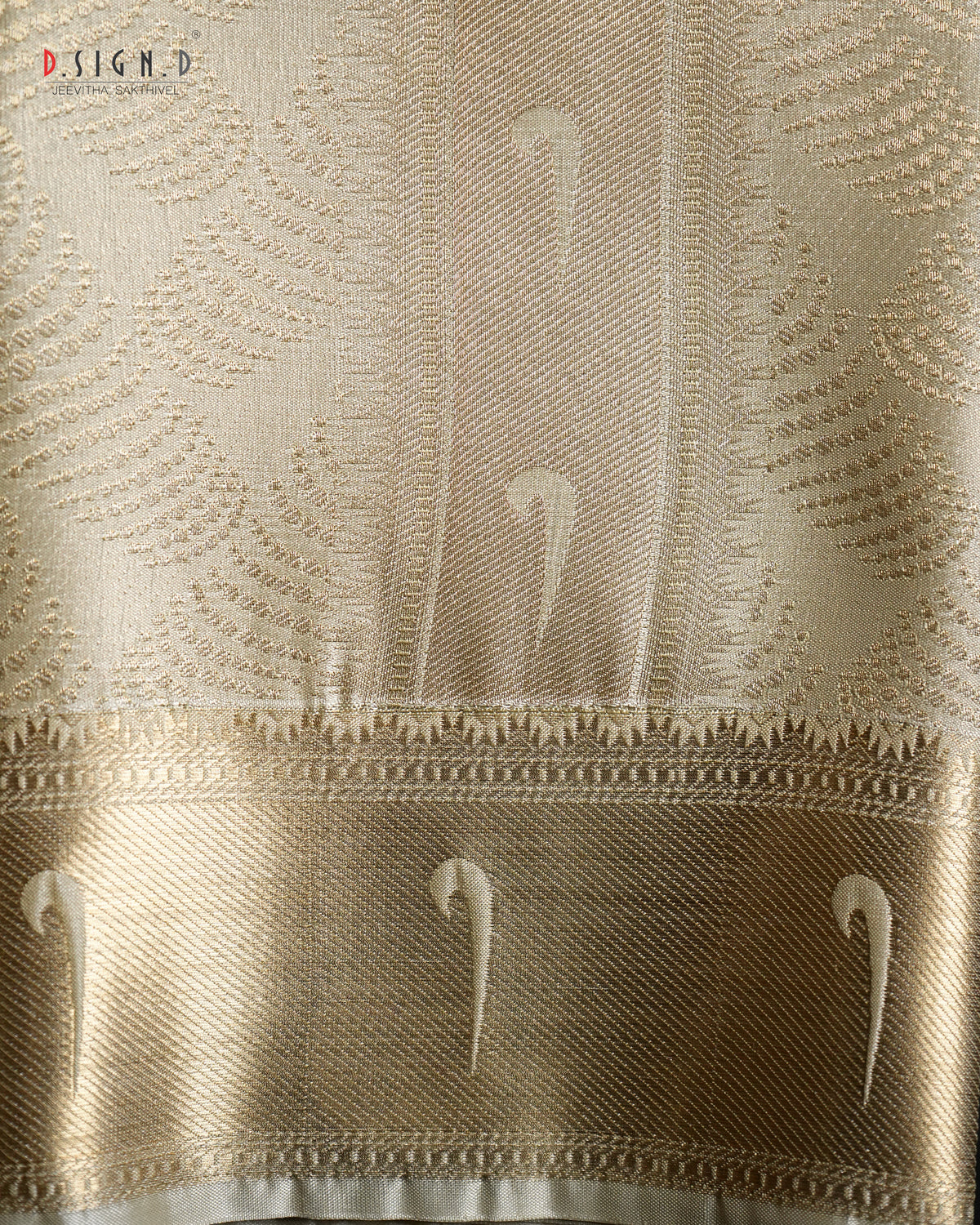 A close-up of a woven fabric with an intricate pattern, featuring a wide metallic gold border with stylized white motifs. 