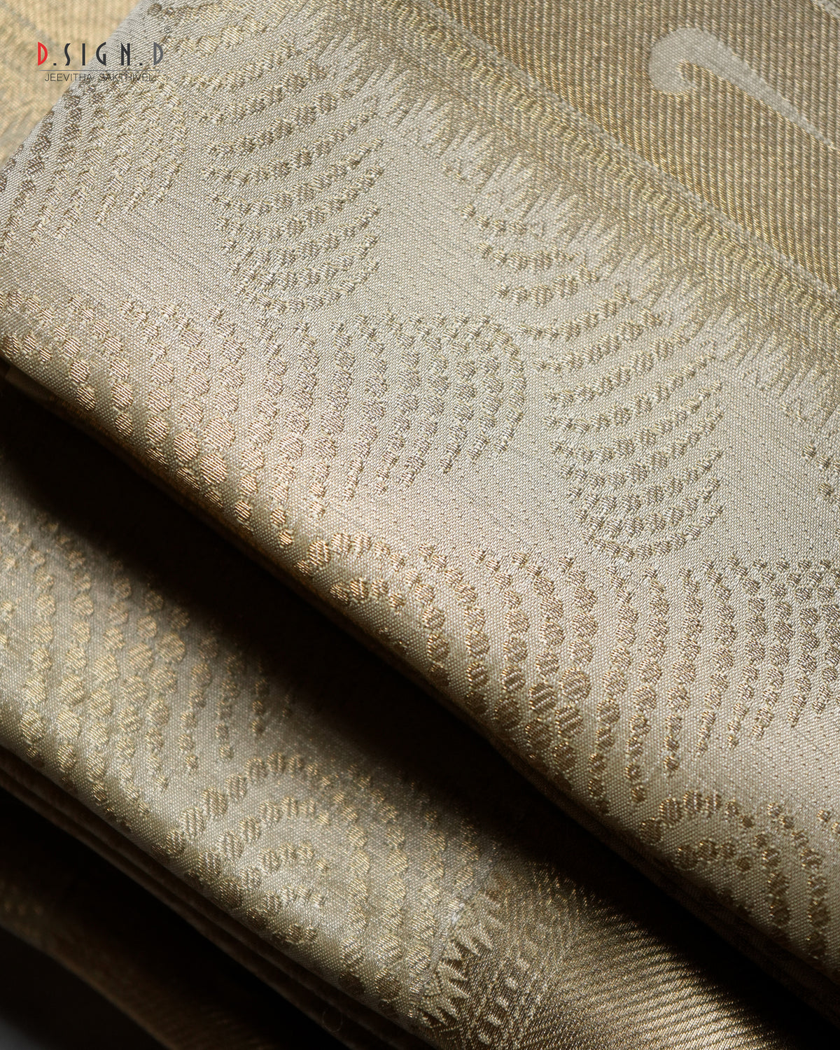 A close-up of folded woven fabric in a warm beige or champagne tone with a subtle repeating textured pattern and sheen. 