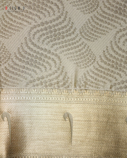 Close-up of a beige and gold patterned fabric, showing a textured upper section with repeating leaf-like motifs and a smoother decorative border below.