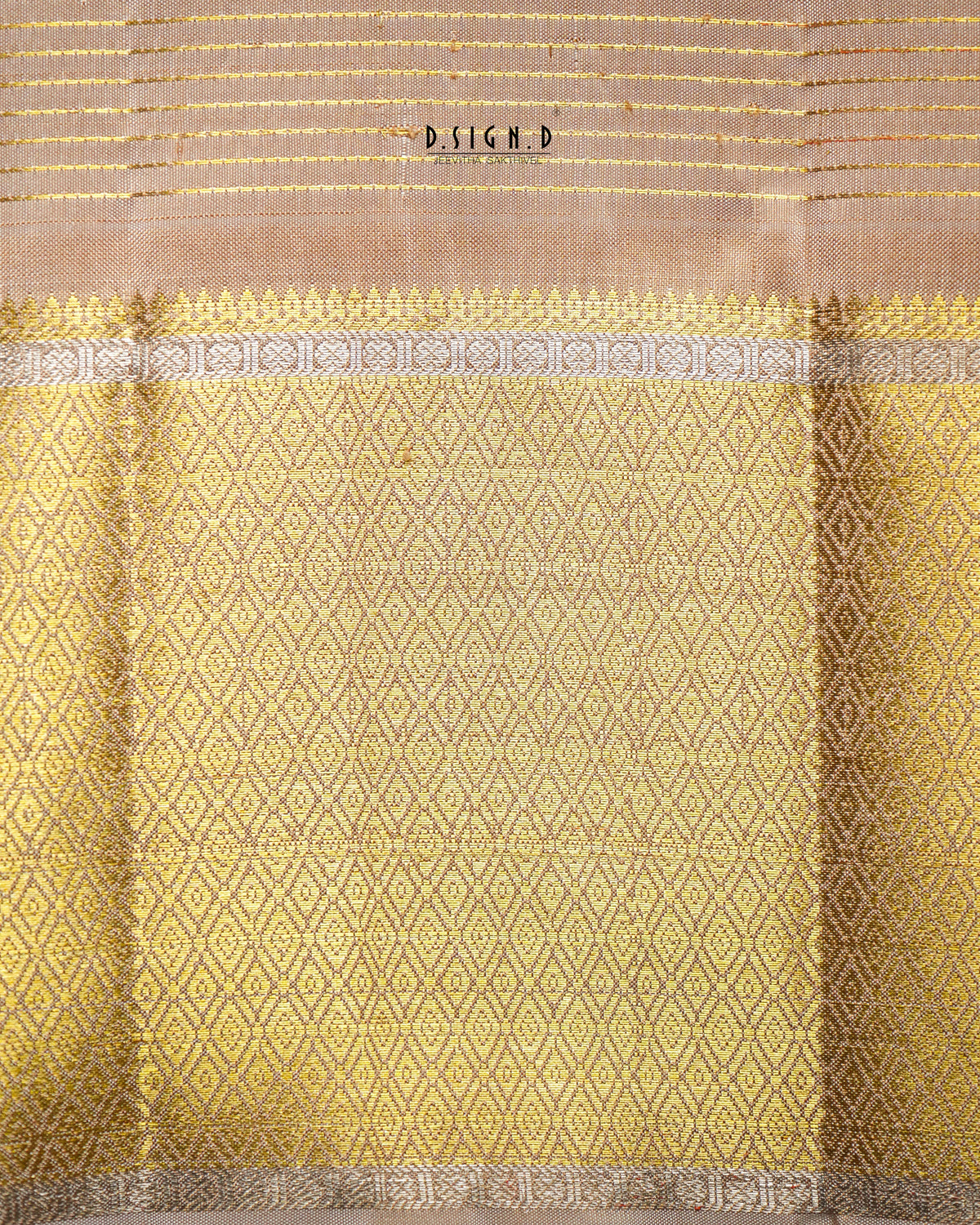 A close-up of a woven textile, likely a dhoti, featuring a golden-yellow body with a repeating diamond pattern, a beige border with gold stripes, and a decorative band of gray and gold motifs. 