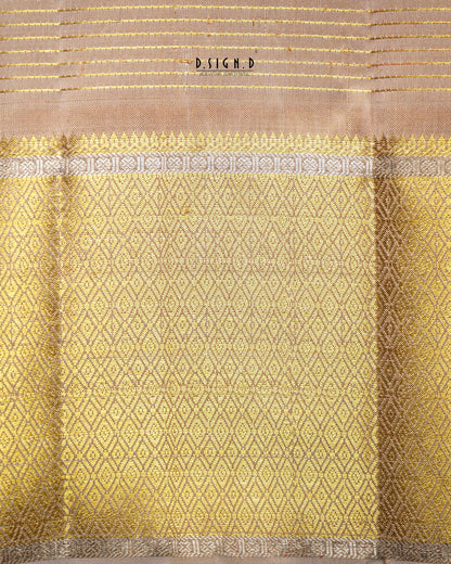 A close-up of a woven textile, likely a dhoti, featuring a golden-yellow body with a repeating diamond pattern, a beige border with gold stripes, and a decorative band of gray and gold motifs. 