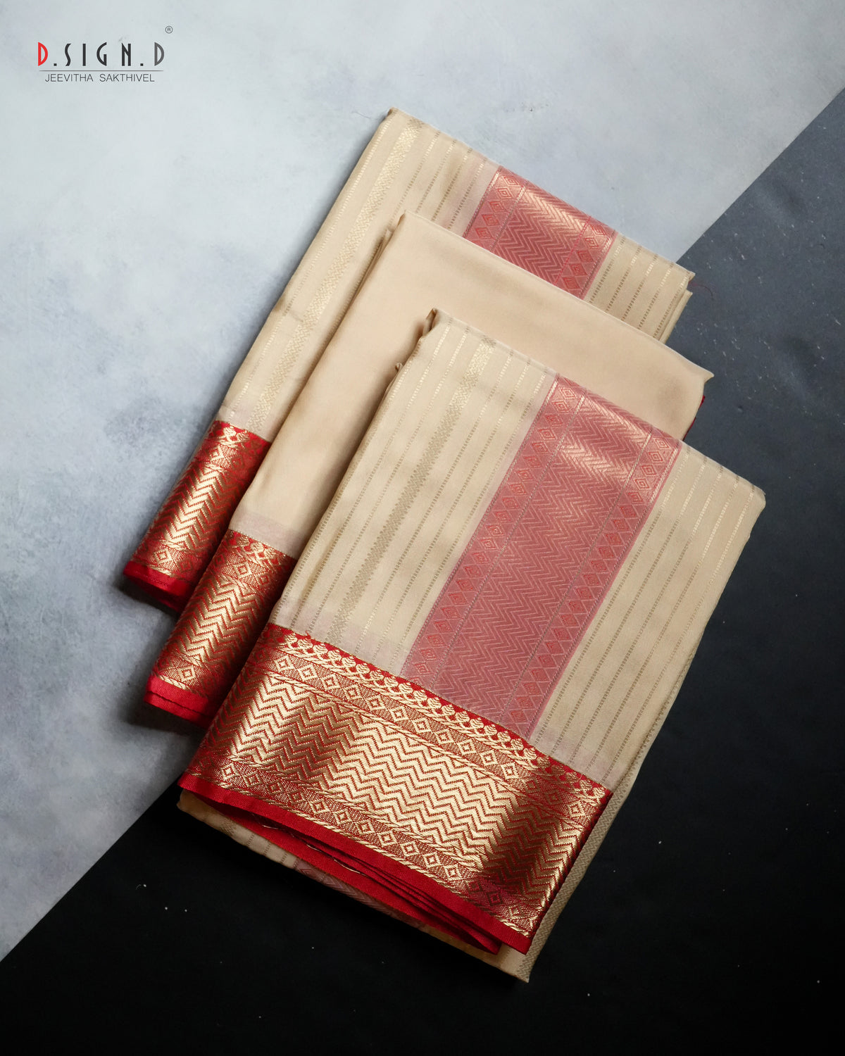 A folded beige and red dhoti, vastram & shirt bit with intricate gold zari metallic borders, displayed diagonally on a split gray and black background. 